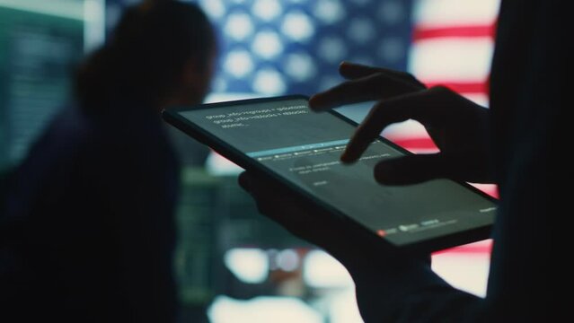 Cybersecurity expert in a governmental IT environment with the American flag. Monitoring cybersecurity, encryption and data security on a tablet to protect against cyber threats. Close up. Camera A.