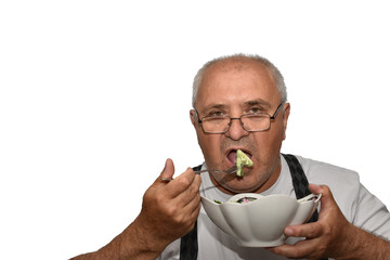 Portrait of an elderly man holding a plate in one hand and a fork with which he is eating in the...