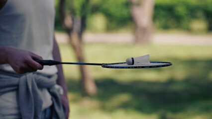 outdoors in a park with trees young handsome brunette guy in jeans and a white T-shirt, a brunette stuffing a shuttlecock warming up before playing bambinton