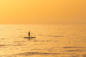 Fototapeta premium A man on his paddleboard in silhouette out in the Mediterranean Sea near Haifa, Israel during the golden hour with a beautiful orange sunset. 