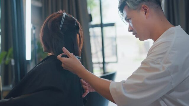 Asian woman getting haircut by hairdresser in the beauty salon, Man hairstylist trimming hair of the customer in a beauty salon.