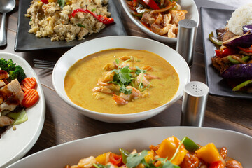 A view of a bowl of yellow curry, among other Asian entrees.