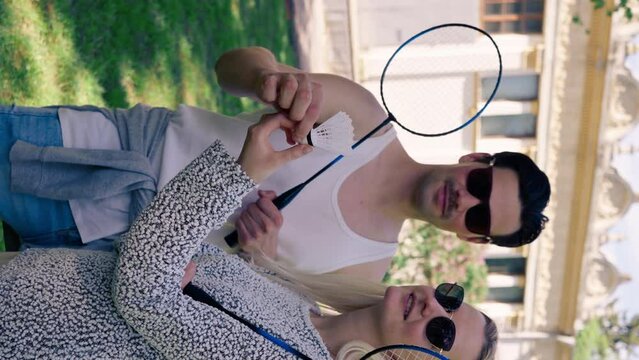 vertical video outdoors in a park with trees young brunette guy stands next to a blonde girl bambinton rackets best friends relaxing together