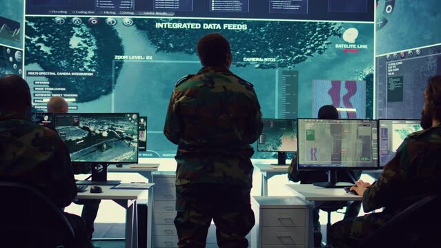 Woman colonel handling a special operation with big data in monitoring room, providing important satellite information to her crew in command post. Targeting enemy power base. Camera B.