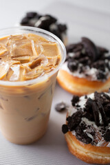 A view of an iced coffee latte beverage next to some cookies and cream donuts.
