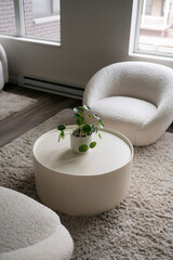 Modern living room with round white table, plant, and cozy chairs.