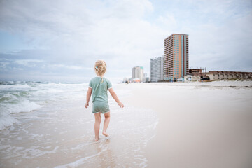 Child wading along beach on Gulf Coast with hotels in background