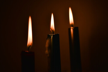 Three candles burn in a row on a dark background.