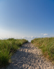 Sandy beach path with foot prints leading to clear blue sky