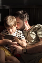 Son and dad are having a great time together. They are looking at the smartphone together and hugging. Concept of a happy childhood and parenthood.