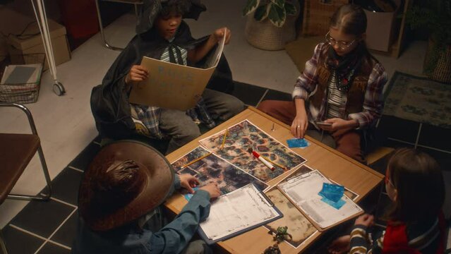 Top view of multiethnic children in costumes gathered at home in evening for role playing game. Girl distributing cards to players