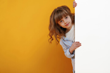 Hiding behind yellow background for copy space. Cute little girl is in the studio