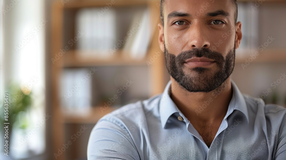 Poster a man with a beard and a blue shirt is standing in front of a bookshelf. he is looking directly at t