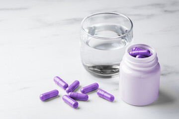 Purple pill capsules with bottle and glass of water, melatonin, supplement, vitamin concept on white background