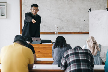 Male teacher angry and pointing to student sitting with head down in the classroom