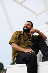 Cheerful african american man holding sunglasses while sitting on lifeguard tower on beach