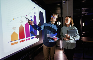 Conception of profit. Man and woman are standing near projector with business data, cooperation