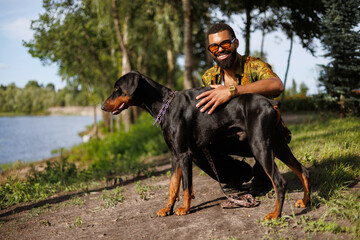 Cheerful young african american man hugging doberman dog in summer park