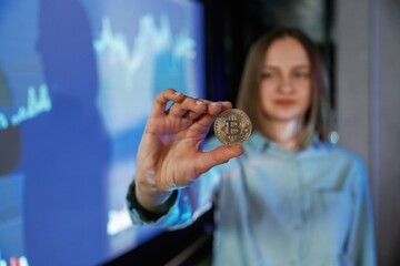 Close up of digital currency coin in hand. Businesswoman is against projector with graphs, indoors