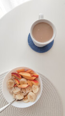 a bowl of oat meal and cup of coffee with milk on the white table in the morning