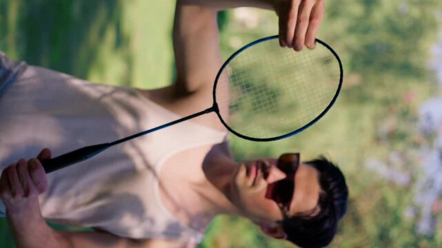 vertical video outdoors in a park with trees young brunette boy standing with a bambinton racket trying to tighten the strings on the racket