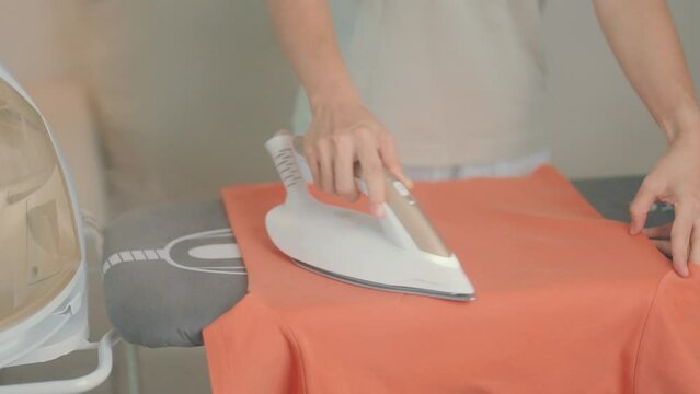 Woman hold Electric hot iron press T shirt clothes on ironing board, Intelligent automatic steam iron. Laundry, Housework, Housekeeping, Domestic hygiene, household of chores and daily routine concept