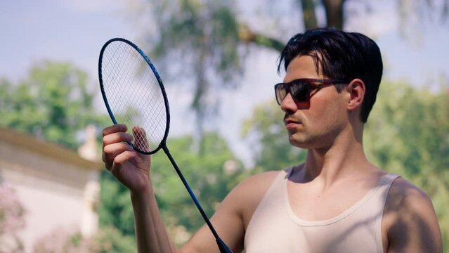 outdoors in a park with trees young brunette boy standing with a bambinton racket trying to tighten the strings on the racket