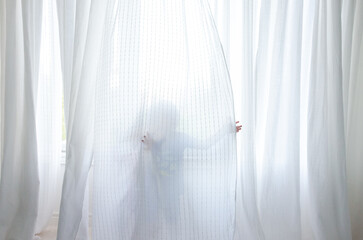 A child playing behind sheer white curtains, partially visible fabric