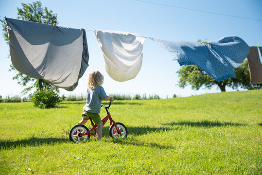 child riding a bike under a laundry line with clean sheets