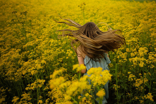 Back view young girl twirling in yellow field of flowers