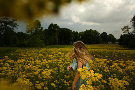 Side view young girl twirling in field of yellow flowers