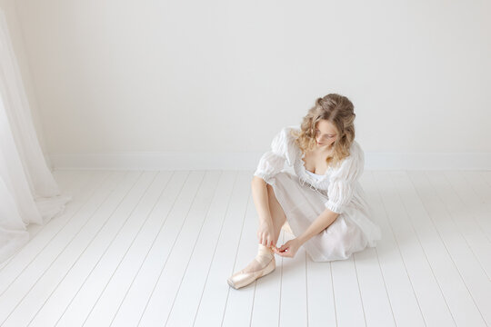 ballerina sits on ground to remove her ballet pointe shoes