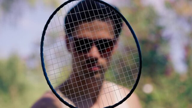 outdoors in a park with trees young brunette boy standing with a bambinton racket trying to tighten the strings on the racket