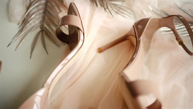 A beige pair of strappy heels near a bag on a piece of tulle