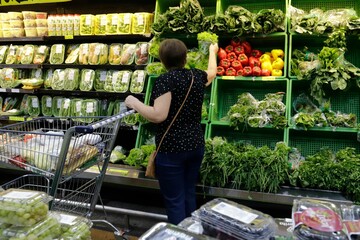Woman shopping for fresh vegetables in a supermarket, reaching for leafy greens in Brazil
