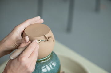 Fototapeta premium A potter works with a tool on a potter's wheel. Close-up of a man's hands. 