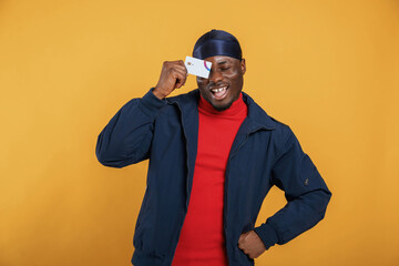 Covering eye by credit card. Handsome black man is in the studio against yellow background