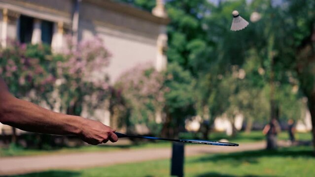 outdoors in a park with trees young handsome brunette guy in jeans and a white T-shirt, a brunette stuffing a shuttlecock warming up before playing bambinton