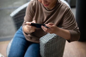 A happy, positive Asian woman is relaxing at an outdoor lounge and using her smartphone.