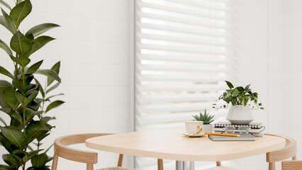 A table by the window in a white room features a coffee cup, books, eyeglasses, and decor plants.