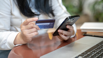 A woman holding her smartphone and credit card at a table outdoors, using her mobile banking app.