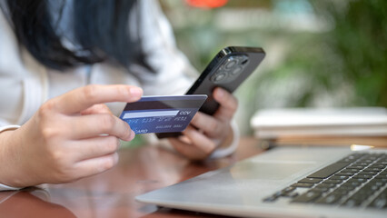 A woman holding her smartphone and credit card at a table outdoors, using her mobile banking app.