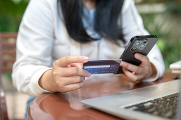 A woman holding her smartphone and credit card at a table outdoors, using her mobile banking app.