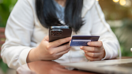 A woman holding her smartphone and credit card at a table outdoors, using her mobile banking app.