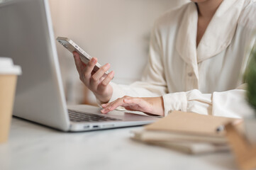 A businesswoman working remotely from a cafe, working on her laptop while using her smartphone.