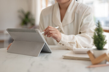 A woman holding a stylus pen and using her digital tablet, working remotely from a cafe.