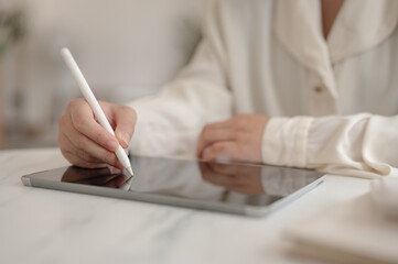 A woman working remotely from a cafe, holding a stylus pen and working on her digital tablet.