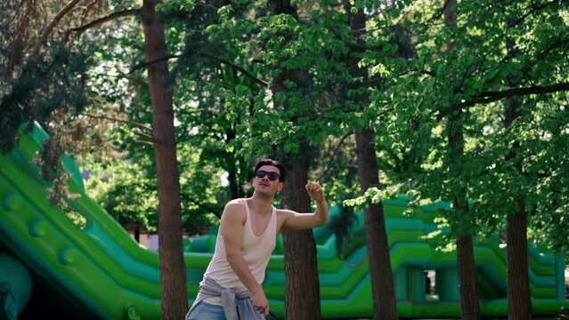 outdoors in a park with trees young handsome brunette guy in jeans and a white T-shirt, a brunette stuffing a shuttlecock warming up before playing bambinton