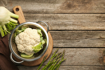 Metal colander with cauliflower, fennel and asparagus on wooden table, flat lay. Space for text