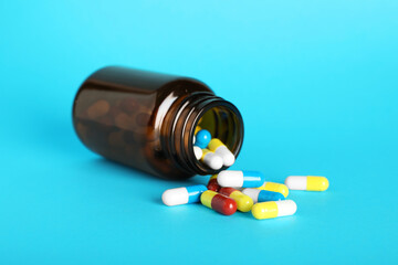 Scattered antibiotic pills and bottle on light blue background. Medicinal treatment